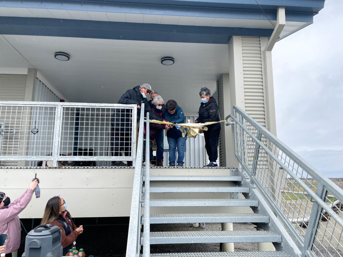 Four people standing at the top of a staircase at the exterior of a clinic. They are together cutting a ribbon tied at the top of the stairs.