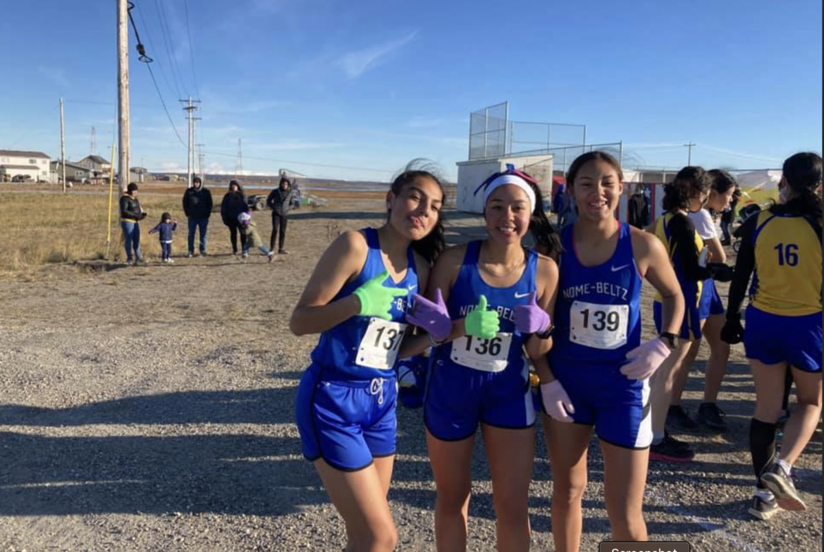 Three Nome girl athletes posing for a picture outside in the track uniforms.