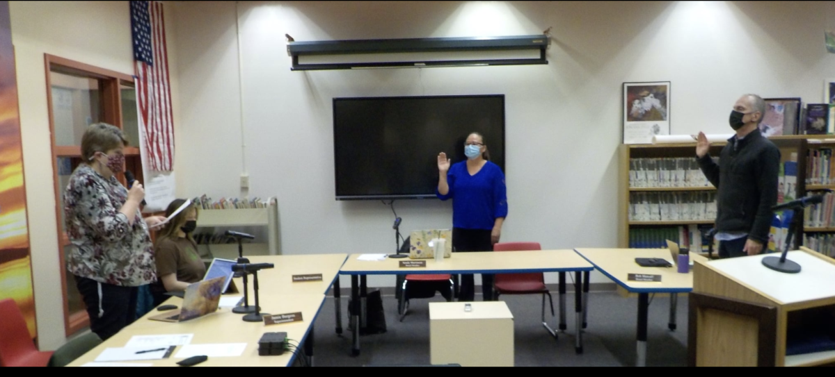 In a room 3 masked people stand facing a woman holding her right hand up.