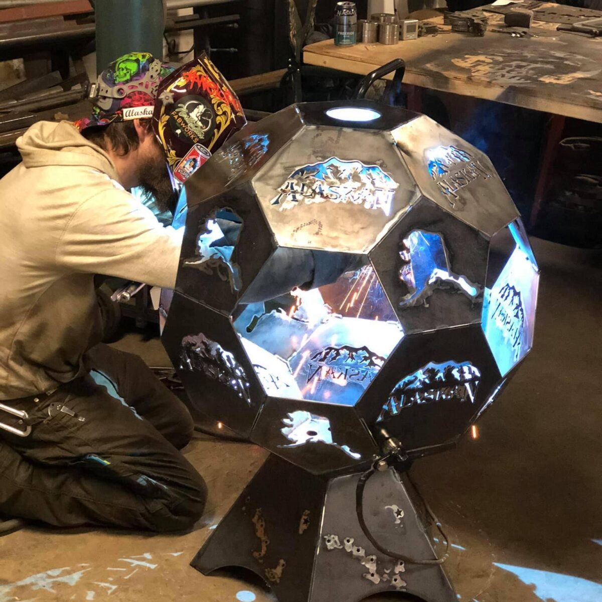A man with welding mask kneeling down and working on a round metal object.
