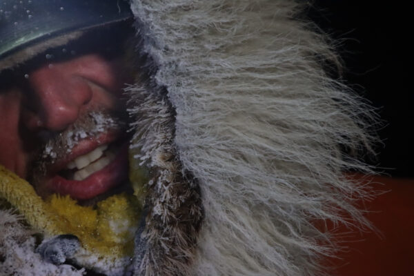 Close up photo of exhausted man. He is wearing a fur hood with ice/snow covering his head