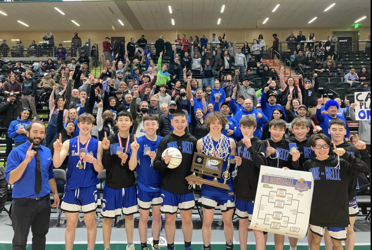A team of highschool basketball boys posing with medals and trophy in gym. Crowd is behind