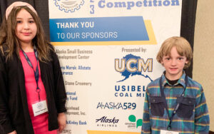 A girl, Denali Walrath, and a boy, Bradley Rowe, stand in front of a banner.