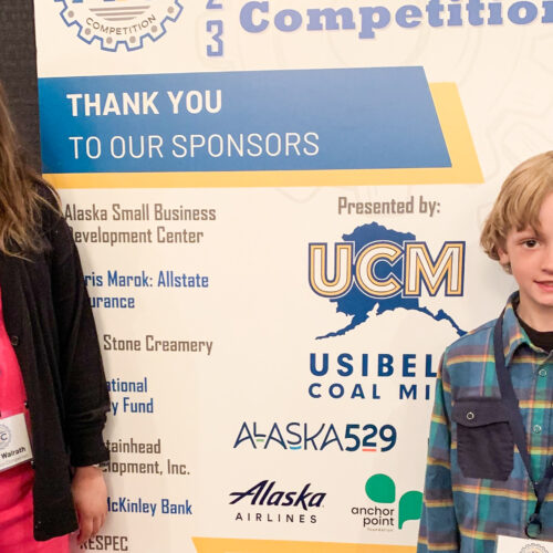 A girl, Denali Walrath, and a boy, Bradley Rowe, stand in front of a banner.
