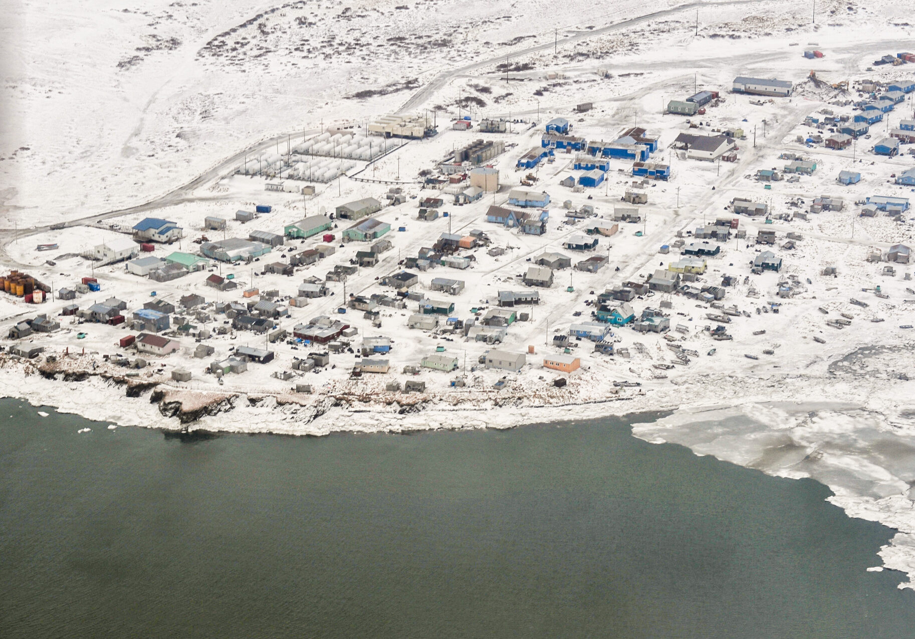 An aerial view over a snowy, coastal Alaska village in wintertime